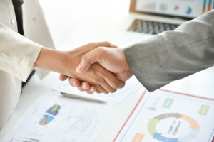 Geschäftlicher Handschlag über Unterlagen und Diagrammen als Symbol für Vertrauen, Partnerschaft und ISO-Beratung.
